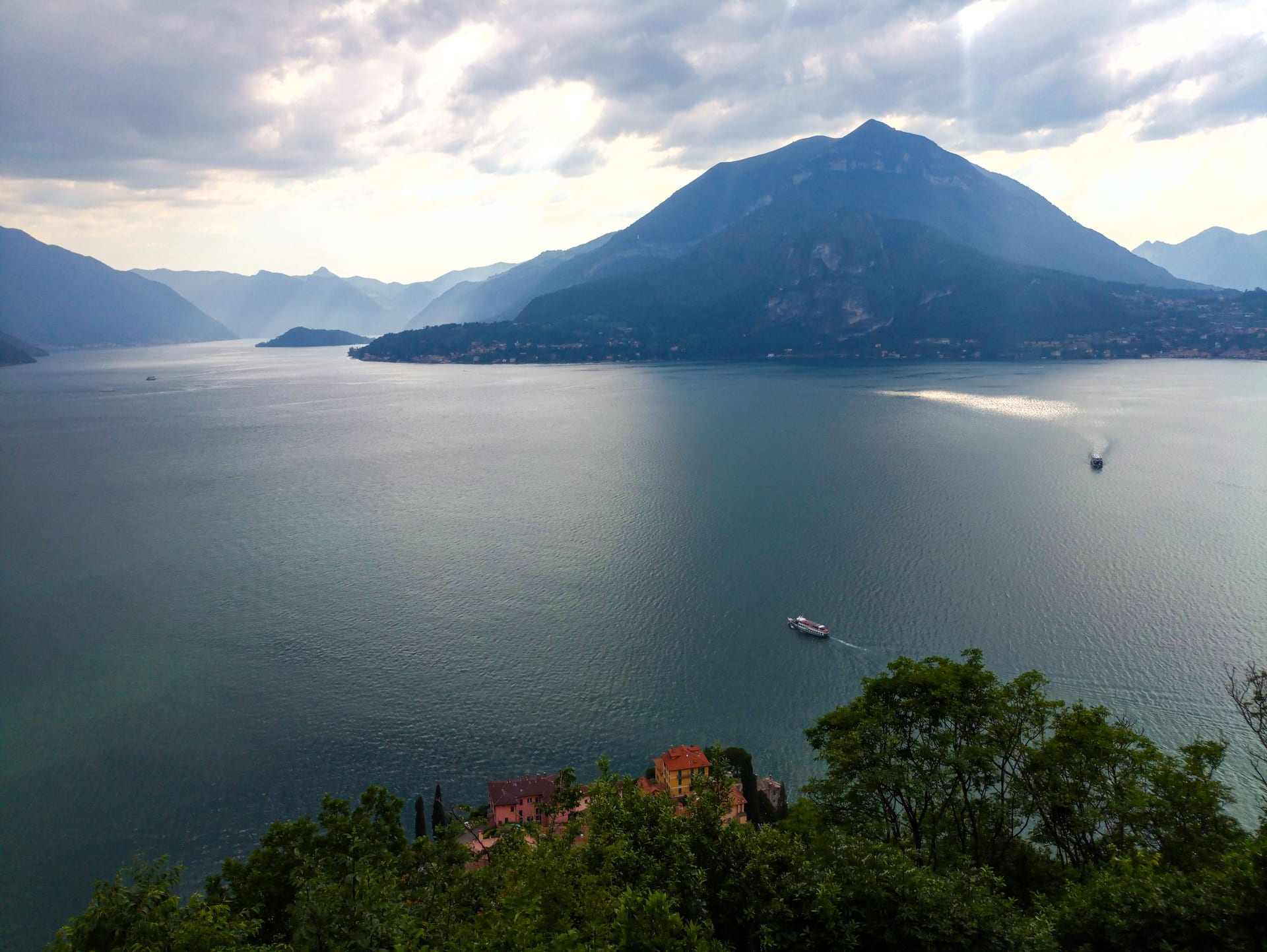 Vista del Lago di Como sotto un cielo nuvoloso, con le montagne e un battello in transito