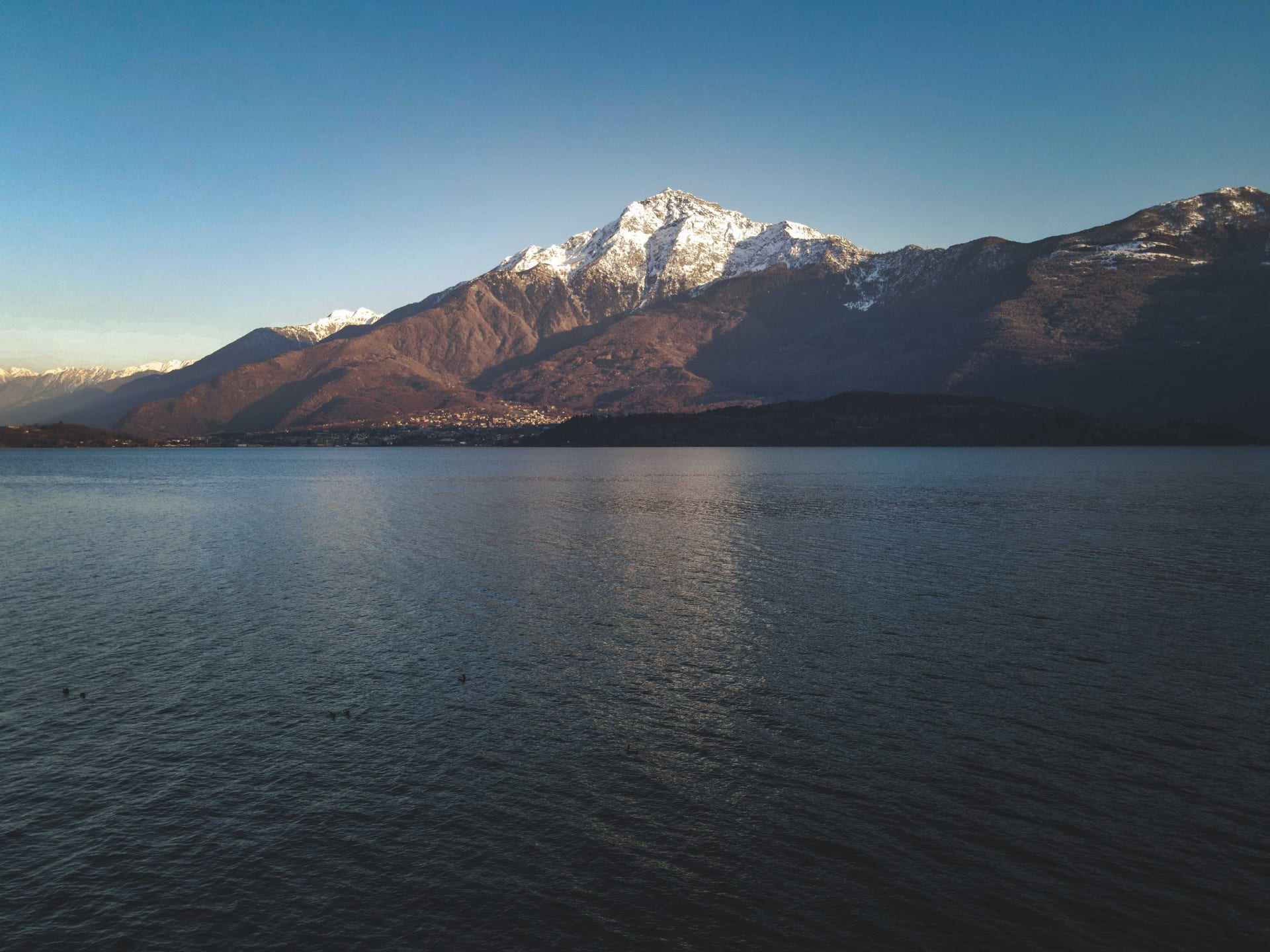 Il Monte Legnone innevato riflesso nelle acque del Lago di Como sotto un cielo limpido
