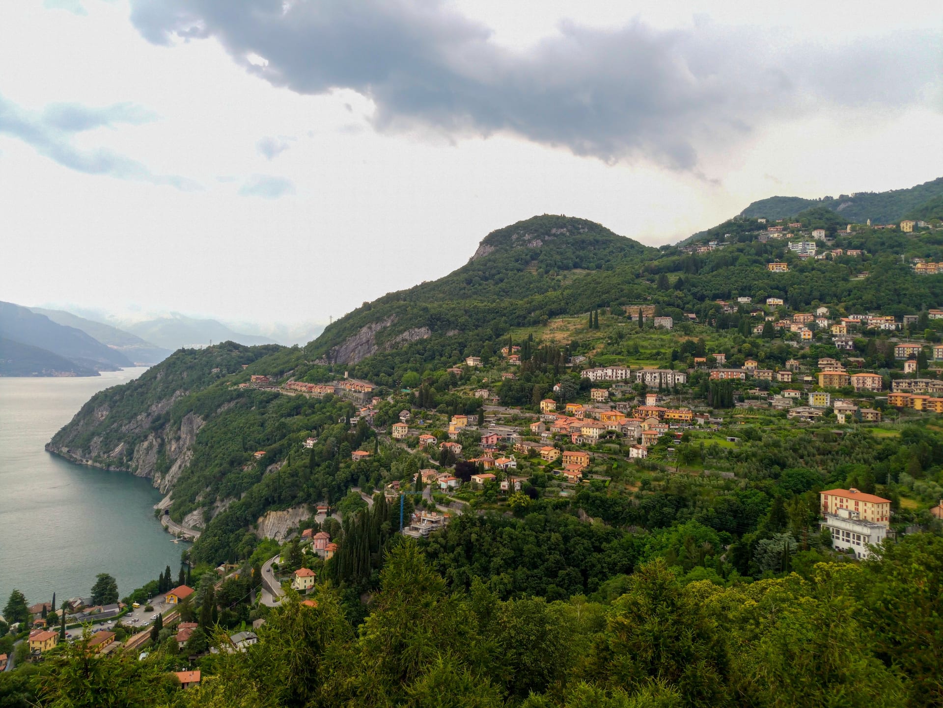 Paesi sul versante verde affacciati sul Lago di Como, visti dall'alto sotto un cielo nuvoloso